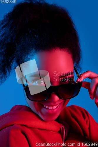 Image of African-american woman\'s portrait isolated on blue studio background in multicolored neon light