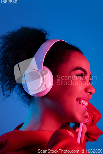 Image of African-american woman\'s portrait isolated on blue studio background in multicolored neon light