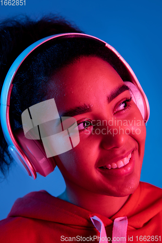 Image of African-american woman\'s portrait isolated on blue studio background in multicolored neon light