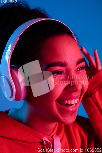Image of African-american woman\'s portrait isolated on blue studio background in multicolored neon light