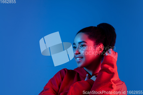 Image of African-american woman\'s portrait isolated on blue studio background in multicolored neon light