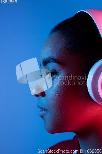 Image of African-american woman\'s portrait isolated on blue studio background in multicolored neon light