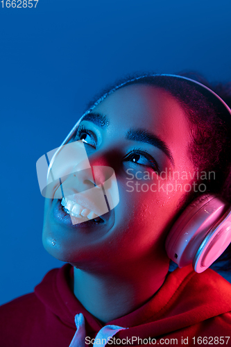 Image of African-american woman\'s portrait isolated on blue studio background in multicolored neon light