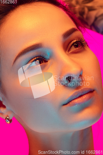 Image of Caucasian beautiful woman\'s portrait isolated on pink studio background in multicolored neon light