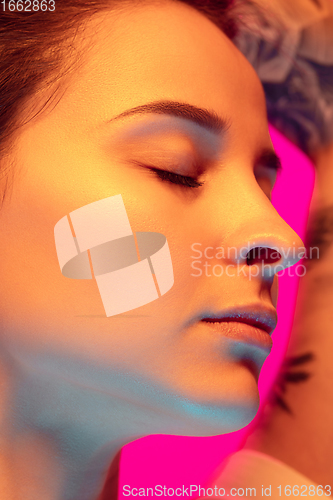 Image of Caucasian beautiful woman\'s portrait isolated on pink studio background in multicolored neon light