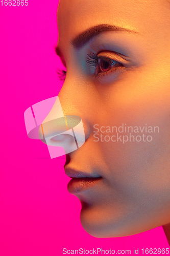 Image of Caucasian beautiful woman\'s portrait isolated on pink studio background in multicolored neon light