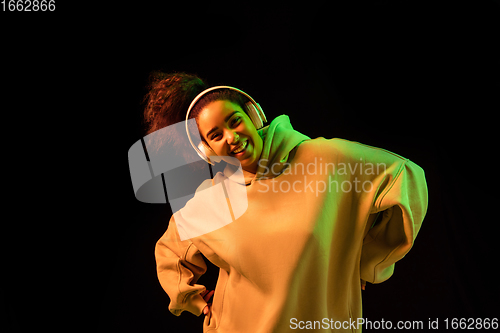 Image of African-american woman\'s portrait isolated on dark studio background in orange-green neon light