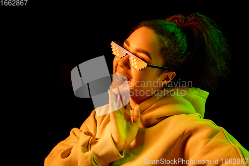 Image of African-american woman\'s portrait isolated on dark studio background in multicolored neon light