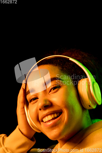 Image of African-american woman\'s portrait isolated on dark studio background in orange-green neon light
