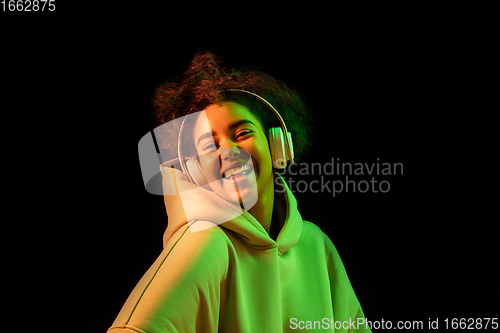 Image of African-american woman\'s portrait isolated on dark studio background in orange-green neon light