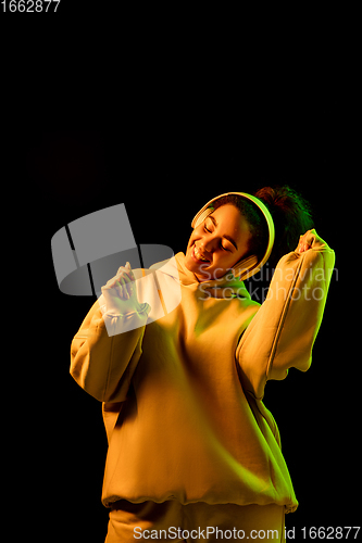Image of African-american woman\'s portrait isolated on dark studio background in orange-green neon light