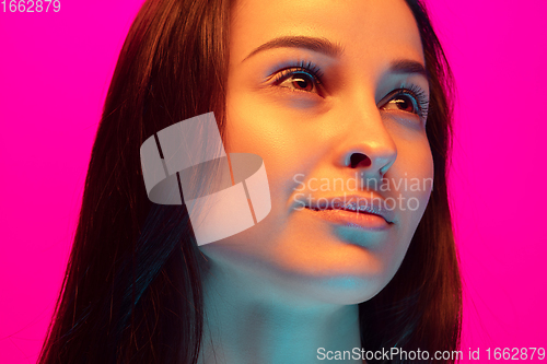 Image of Caucasian beautiful woman\'s portrait isolated on pink studio background in multicolored neon light