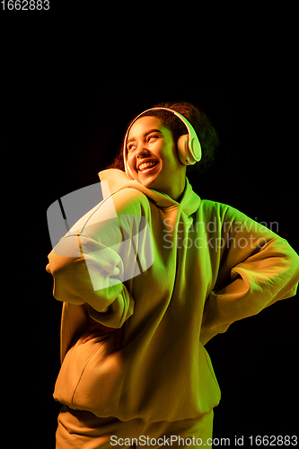 Image of African-american woman\'s portrait isolated on dark studio background in orange-green neon light