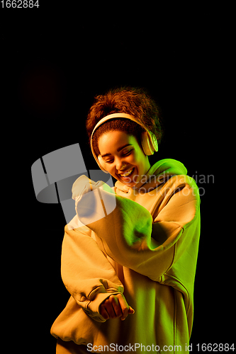 Image of African-american woman\'s portrait isolated on dark studio background in orange-green neon light
