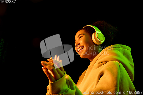 Image of African-american woman\'s portrait isolated on dark studio background in orange-green neon light