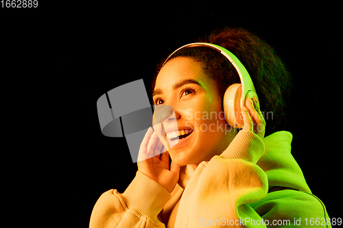 Image of African-american woman\'s portrait isolated on dark studio background in orange-green neon light