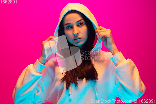 Image of Caucasian beautiful woman\'s portrait isolated on pink studio background in multicolored neon light