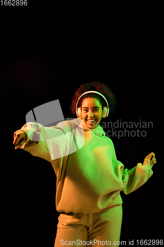 Image of African-american woman\'s portrait isolated on dark studio background in orange-green neon light