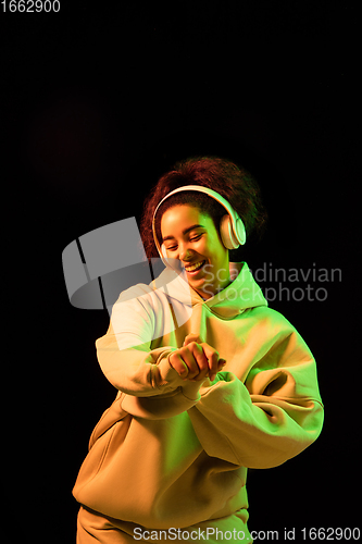 Image of African-american woman\'s portrait isolated on dark studio background in orange-green neon light