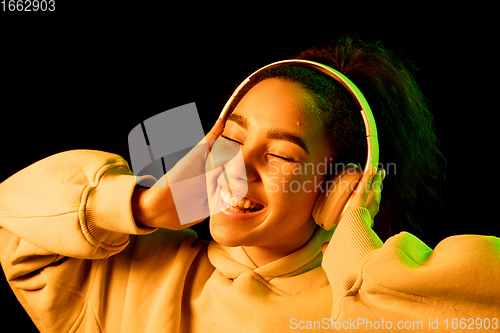 Image of African-american woman\'s portrait isolated on dark studio background in orange-green neon light