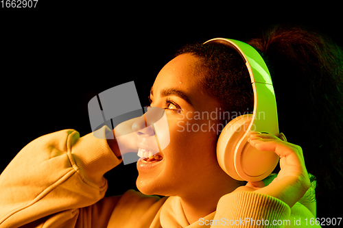 Image of African-american woman\'s portrait isolated on dark studio background in orange-green neon light