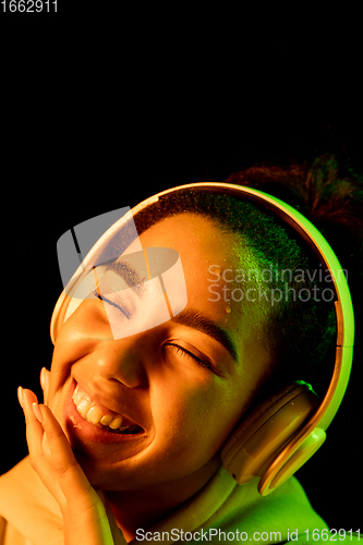 Image of African-american woman\'s portrait isolated on dark studio background in orange-green neon light