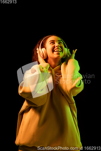 Image of African-american woman\'s portrait isolated on dark studio background in orange-green neon light