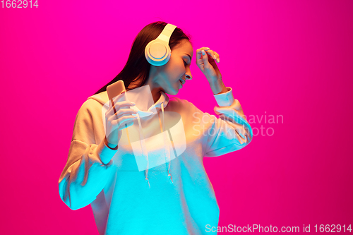 Image of Caucasian beautiful woman\'s portrait isolated on pink studio background in multicolored neon light