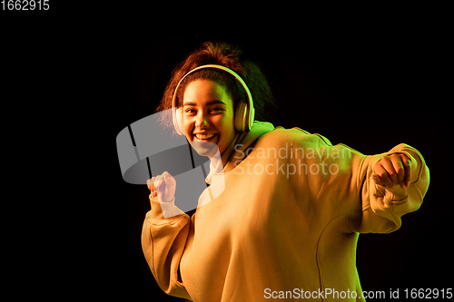 Image of African-american woman\'s portrait isolated on dark studio background in orange-green neon light