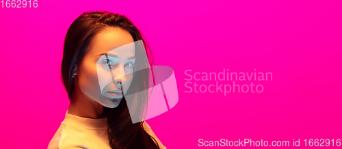 Image of Caucasian beautiful woman\'s portrait isolated on pink studio background in multicolored neon light