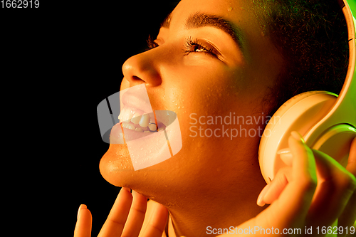 Image of African-american woman\'s portrait isolated on dark studio background in orange-green neon light