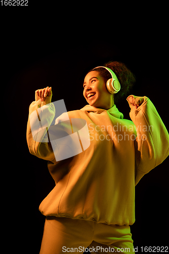 Image of African-american woman\'s portrait isolated on dark studio background in orange-green neon light