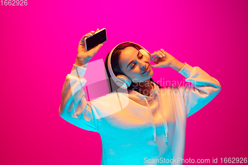 Image of Caucasian beautiful woman\'s portrait isolated on pink studio background in multicolored neon light