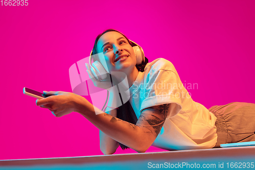 Image of Caucasian beautiful woman\'s portrait isolated on pink studio background in multicolored neon light