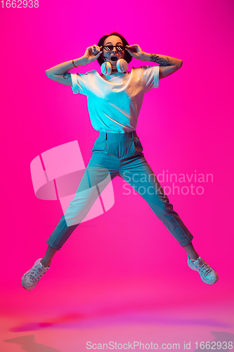 Image of Caucasian beautiful woman\'s portrait isolated on pink studio background in multicolored neon light