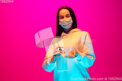 Image of Caucasian beautiful woman\'s portrait isolated on pink studio background in multicolored neon light. Wearing face mask.