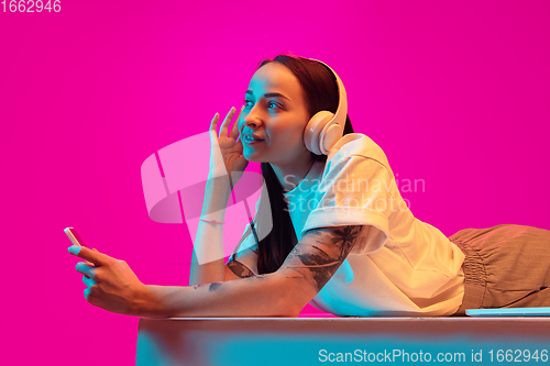 Image of Caucasian beautiful woman\'s portrait isolated on pink studio background in multicolored neon light