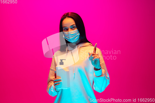 Image of Caucasian beautiful woman\'s portrait isolated on pink studio background in multicolored neon light. Wearing face mask.