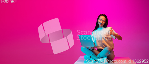 Image of Caucasian beautiful woman\'s portrait isolated on pink studio background in multicolored neon light