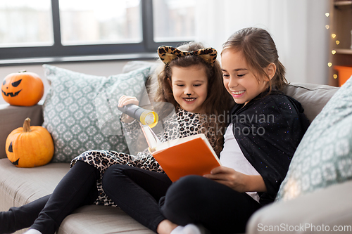 Image of girls in halloween costumes reading book at home