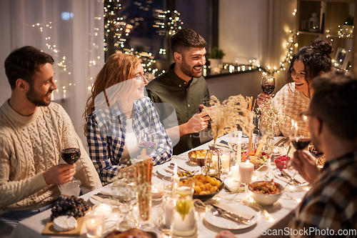 Image of happy friends drinking red wine at christmas party