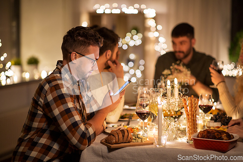 Image of man with smartphone at dinner party with friends