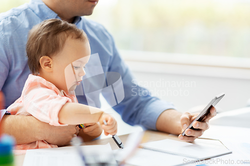 Image of father with baby and smartphone working at home