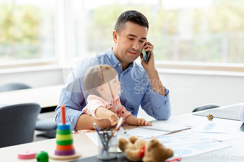 Image of father with baby calling on phone at home office