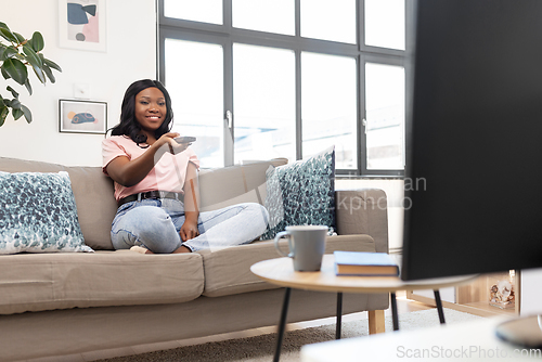 Image of happy african american woman watching tv at home