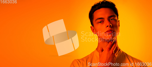 Image of Handsome caucasian man\'s portrait isolated on orange studio background in neon light, monochrome