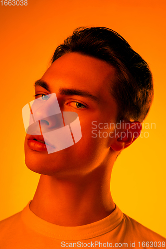 Image of Handsome caucasian man\'s portrait isolated on orange studio background in neon light, monochrome