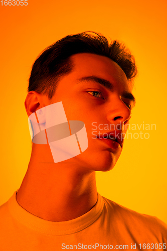 Image of Handsome caucasian man\'s portrait isolated on orange studio background in neon light, monochrome