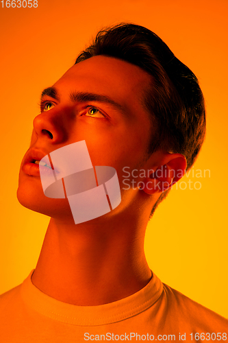 Image of Handsome caucasian man\'s portrait isolated on orange studio background in neon light, monochrome