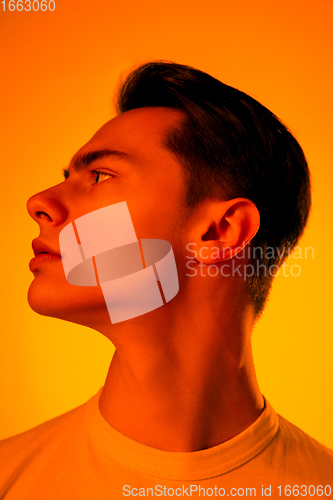 Image of Handsome caucasian man\'s portrait isolated on orange studio background in neon light, monochrome